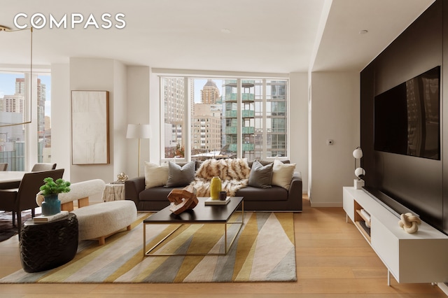 living room with expansive windows, light wood-style floors, a view of city, and baseboards