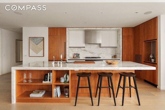 kitchen with brown cabinetry, modern cabinets, wall chimney range hood, white cabinetry, and open shelves