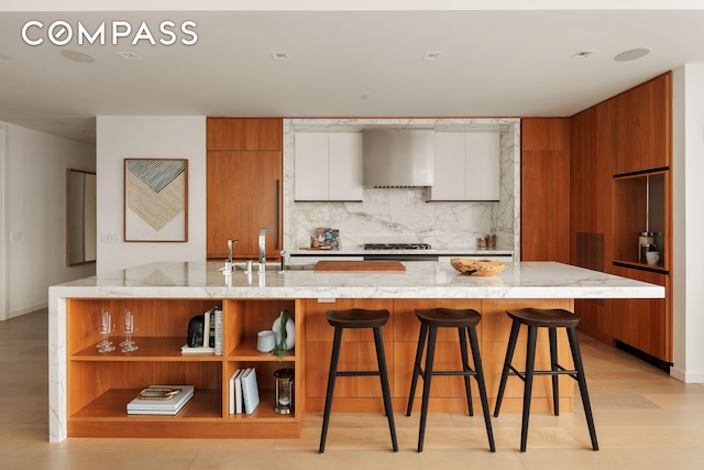 kitchen with brown cabinetry, wall chimney exhaust hood, modern cabinets, open shelves, and backsplash