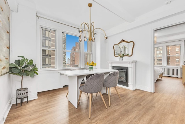 400 E 59th St Unit 9G, New York City, NY 10022 - dining space featuring radiator, light wood-style flooring, beam ceiling, a chandelier, and a glass covered fireplace