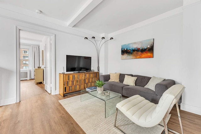 living area featuring beamed ceiling, baseboards, light wood-style flooring, and radiator