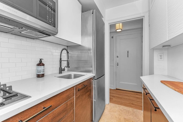 kitchen with brown cabinetry, light countertops, tasteful backsplash, a sink, and stainless steel appliances