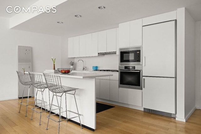 kitchen with built in appliances, light countertops, a kitchen breakfast bar, and white cabinets