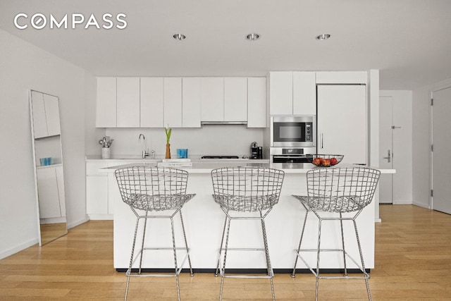 kitchen featuring light countertops, stainless steel microwave, white cabinets, a kitchen island, and light wood-type flooring