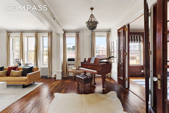 sitting room featuring wood-type flooring, ornamental molding, radiator heating unit, and ornate columns