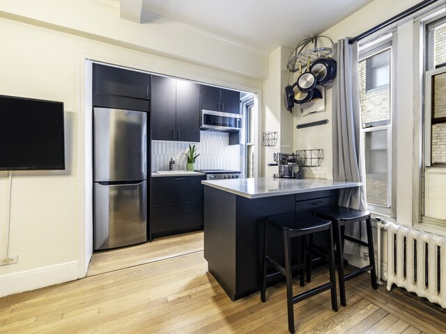 325 W 45th St Unit 404, New York City, NY 10036 - kitchen with stainless steel appliances, dark cabinets, a kitchen bar, and radiator heating unit