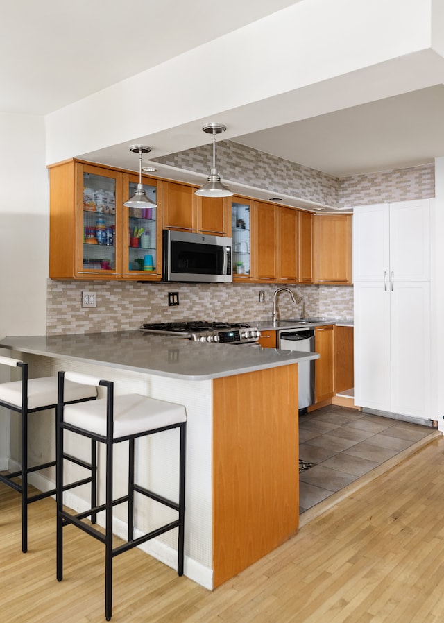 kitchen with stainless steel appliances, a peninsula, light wood-style floors, a kitchen bar, and brown cabinetry