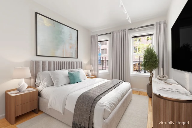 bedroom with light wood-style floors, track lighting, and baseboards