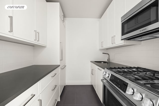 kitchen featuring a sink, white cabinetry, appliances with stainless steel finishes, backsplash, and dark countertops