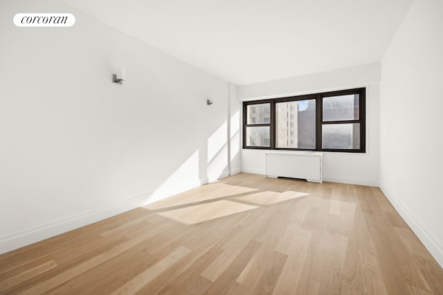 spare room featuring light wood-type flooring, radiator, visible vents, and baseboards