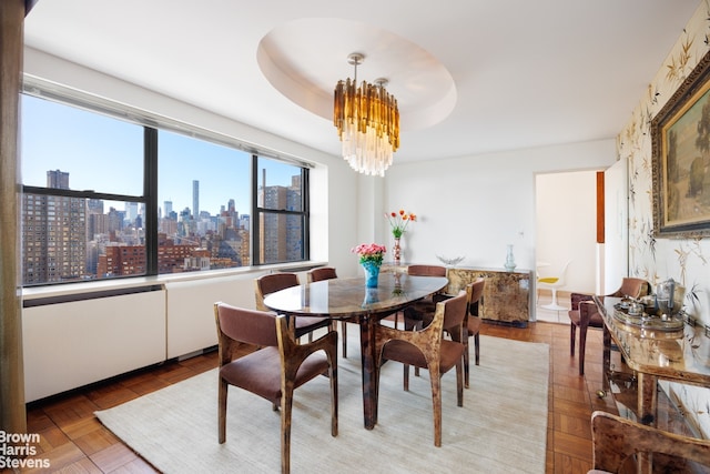 dining space with an inviting chandelier, a raised ceiling, and a city view