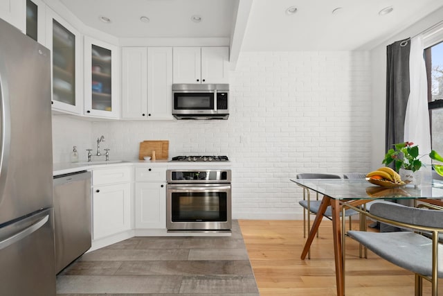 kitchen with a sink, white cabinets, light countertops, appliances with stainless steel finishes, and light wood finished floors