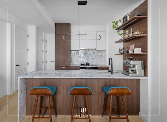 bar featuring tasteful backsplash, light wood-style flooring, and a sink