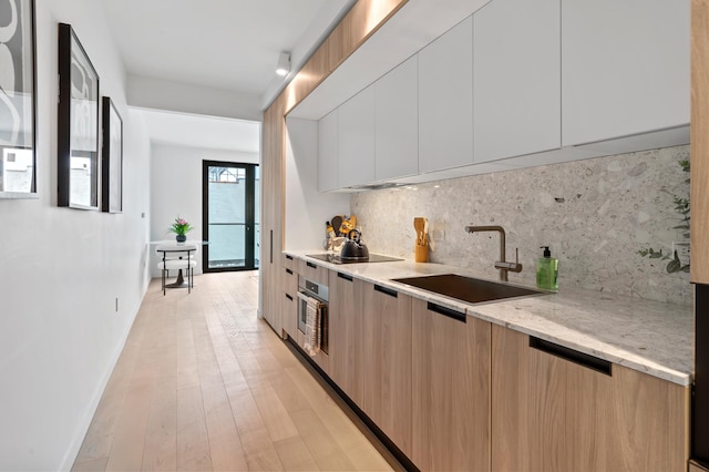 kitchen featuring decorative backsplash, modern cabinets, a sink, baseboards, and stainless steel oven