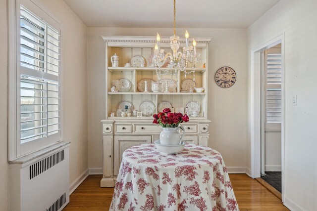 dining space with baseboards, a notable chandelier, light wood finished floors, and radiator heating unit