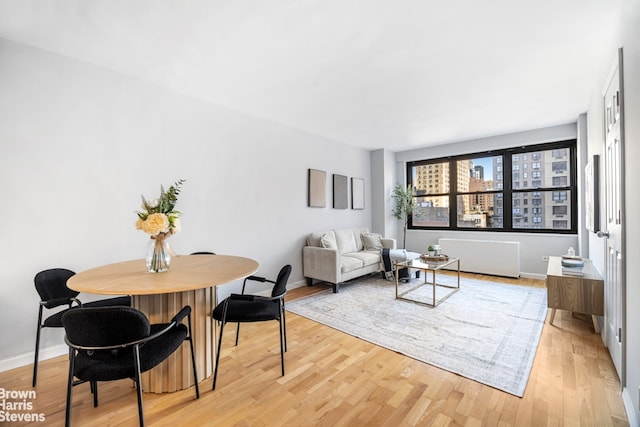 dining room with light wood-type flooring, radiator, baseboards, and a city view