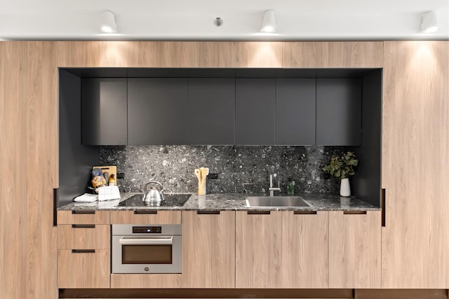 kitchen with dark stone counters, modern cabinets, black electric stovetop, stainless steel oven, and a sink