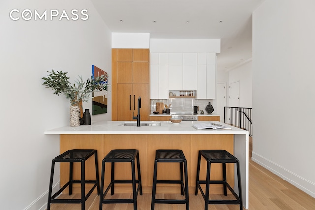 kitchen with tasteful backsplash, light countertops, a peninsula, a kitchen breakfast bar, and a sink