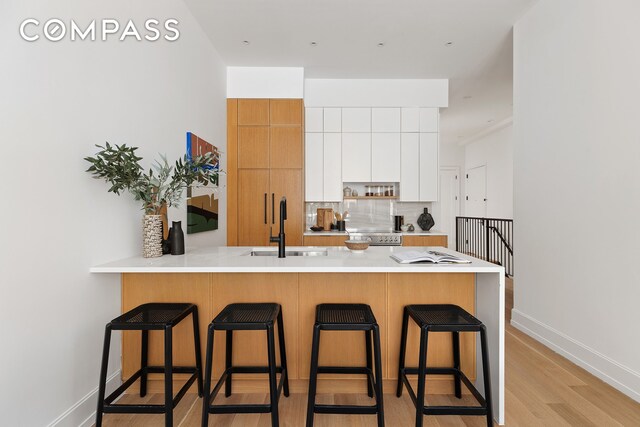 kitchen featuring a sink, a peninsula, a breakfast bar area, light countertops, and decorative backsplash