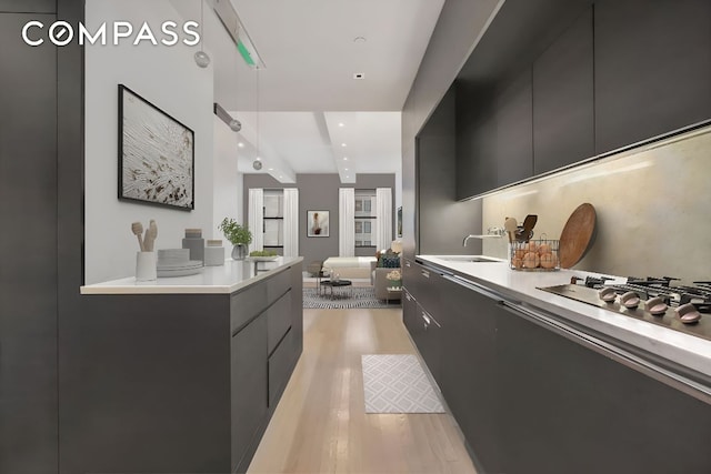 kitchen with sink, stainless steel gas stovetop, light hardwood / wood-style floors, and decorative light fixtures