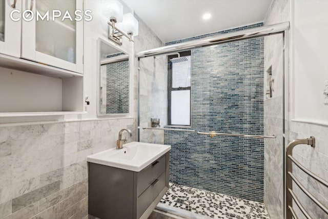 full bath with tile walls, a wainscoted wall, vanity, and a stall shower