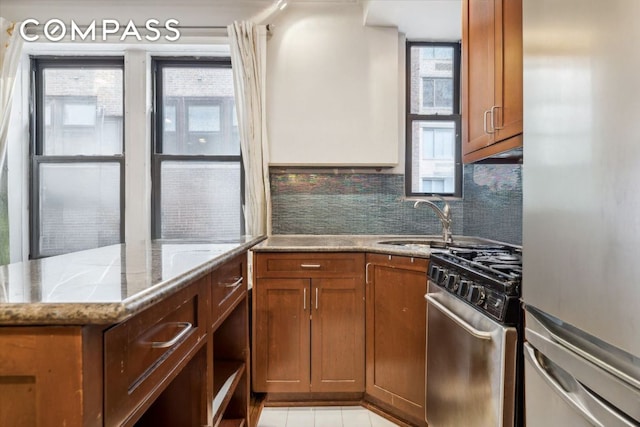 kitchen with appliances with stainless steel finishes, sink, backsplash, light stone counters, and light tile patterned floors