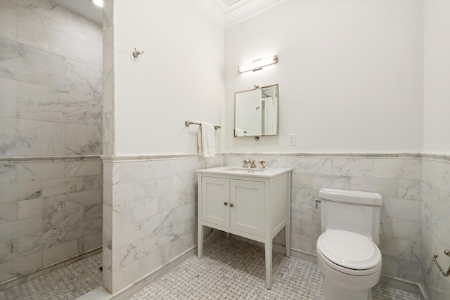 bathroom with crown molding, vanity, wainscoting, toilet, and tile walls