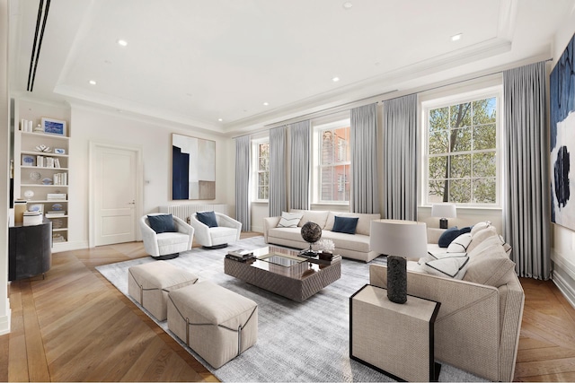 living room with built in shelves, a raised ceiling, ornamental molding, and light wood-style flooring