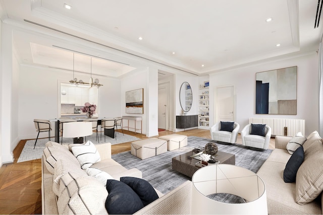 living area with a notable chandelier, a raised ceiling, radiator heating unit, baseboards, and ornamental molding