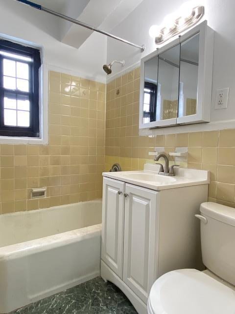 full bathroom with vanity, tile walls, toilet, and tiled shower / bath