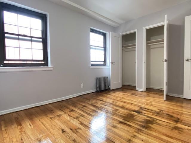 unfurnished bedroom featuring radiator, hardwood / wood-style floors, and two closets