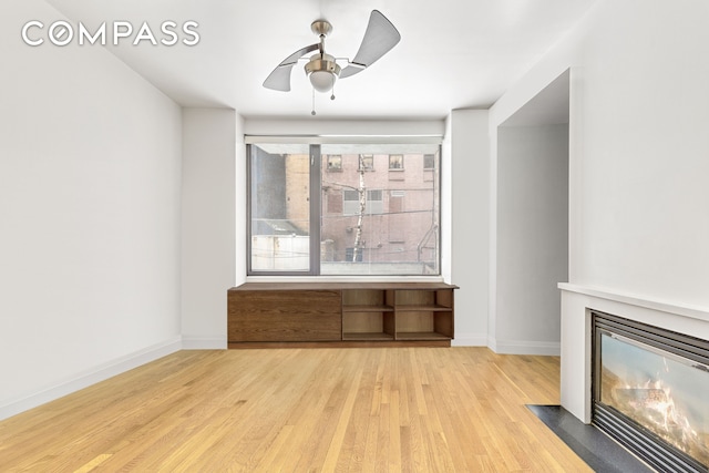 unfurnished living room with a ceiling fan, a fireplace with flush hearth, baseboards, and wood finished floors