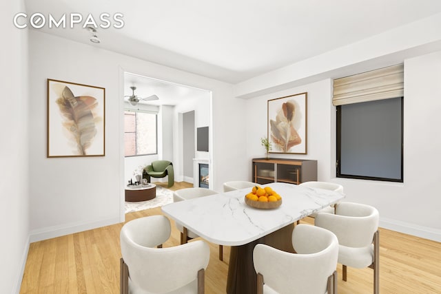 dining room with light wood-type flooring, a glass covered fireplace, and baseboards