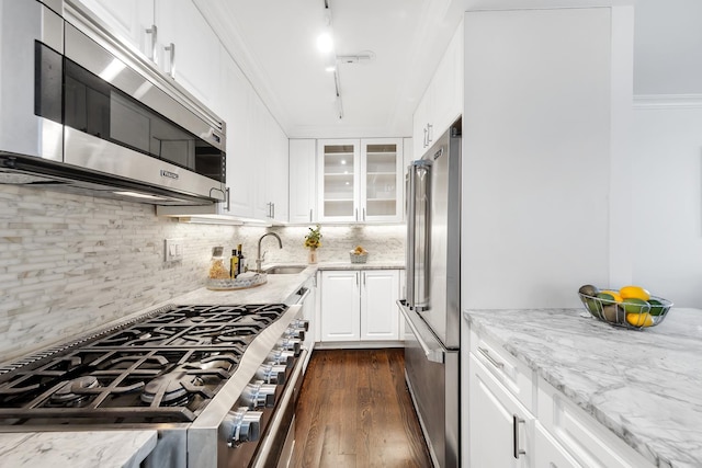 kitchen featuring crown molding, light stone counters, decorative backsplash, stainless steel appliances, and a sink