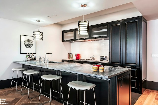 kitchen with a breakfast bar area, dark stone countertops, a sink, and decorative light fixtures