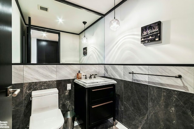 bathroom with toilet, visible vents, tile walls, and vanity