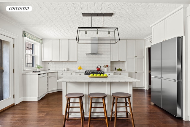 kitchen with appliances with stainless steel finishes, light stone countertops, white cabinets, wall chimney range hood, and a center island