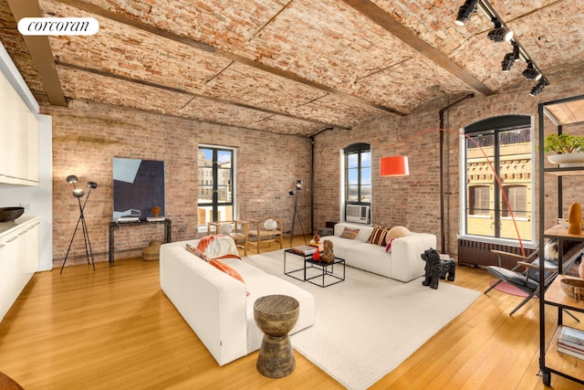 unfurnished living room with track lighting, radiator heating unit, brick wall, brick ceiling, and light wood-type flooring