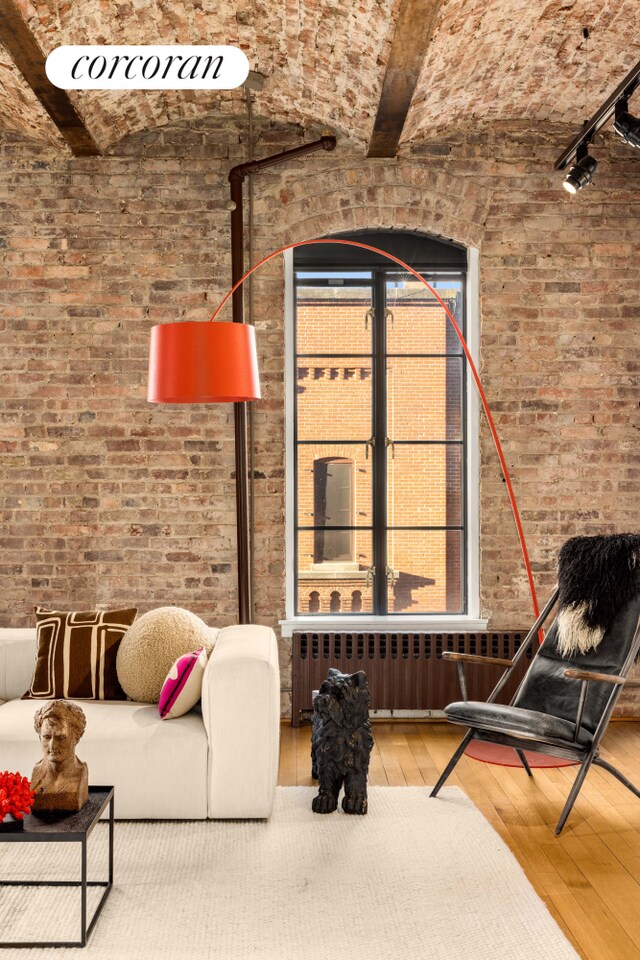 unfurnished room featuring brick ceiling, plenty of natural light, radiator heating unit, and hardwood / wood-style floors