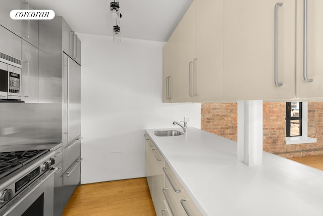 kitchen featuring appliances with stainless steel finishes, sink, brick wall, and light hardwood / wood-style flooring