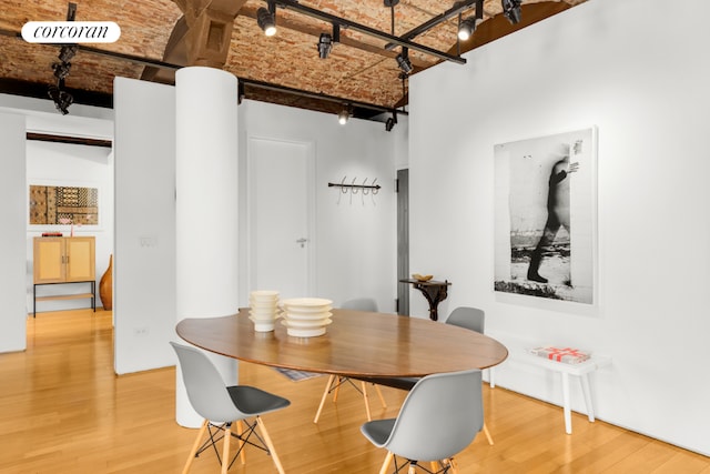 dining room with hardwood / wood-style flooring, rail lighting, a towering ceiling, and brick ceiling