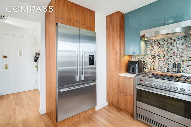 kitchen featuring light wood finished floors, tasteful backsplash, modern cabinets, high quality appliances, and extractor fan