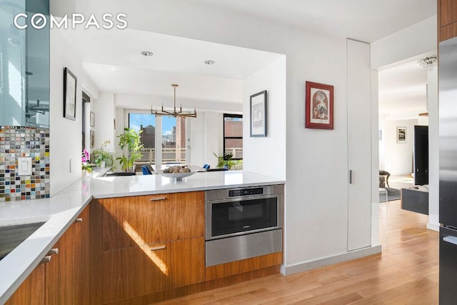 kitchen with oven, light wood-style flooring, light countertops, brown cabinetry, and modern cabinets