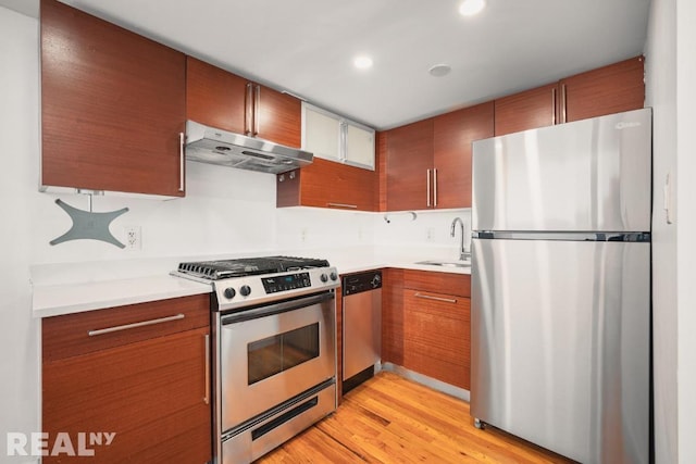 kitchen featuring appliances with stainless steel finishes, light countertops, light wood-type flooring, under cabinet range hood, and a sink