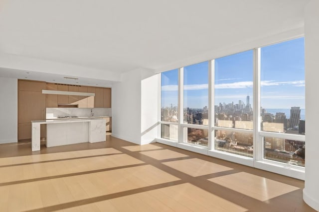 unfurnished living room with a view of city, a wall of windows, light wood-type flooring, and baseboards