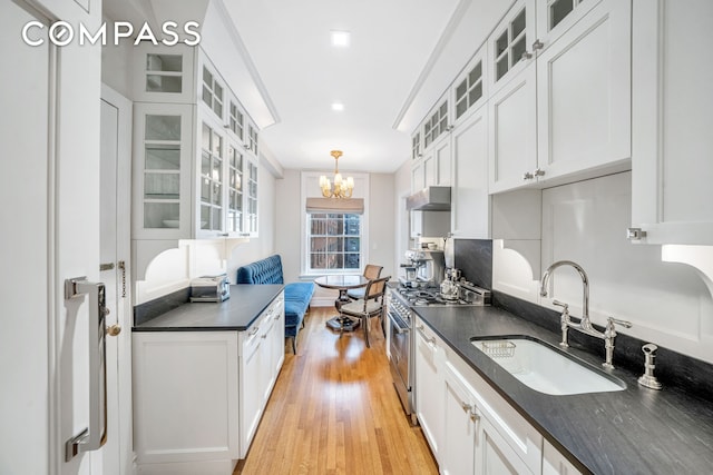 kitchen featuring dark countertops, stainless steel stove, white cabinets, a sink, and under cabinet range hood