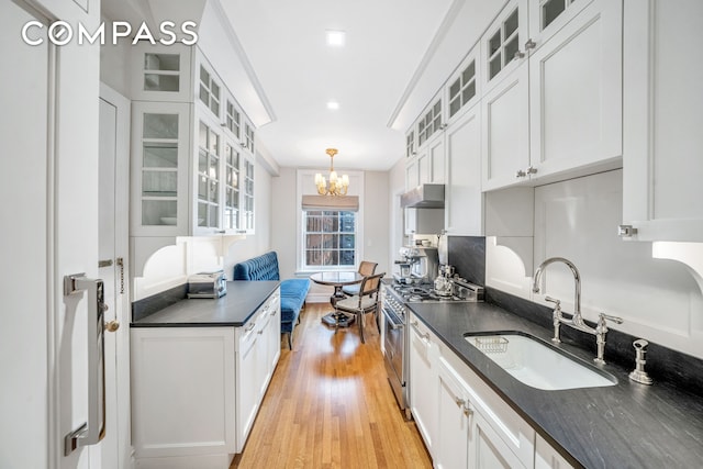 kitchen with dark countertops, stainless steel stove, a sink, a chandelier, and under cabinet range hood