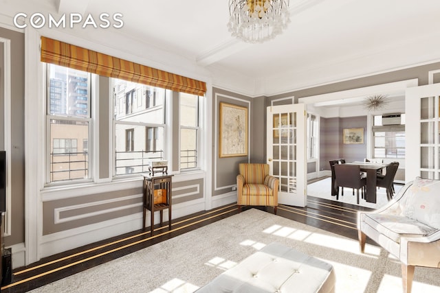 sitting room with beam ceiling, ornamental molding, wood finished floors, a chandelier, and a wall mounted air conditioner