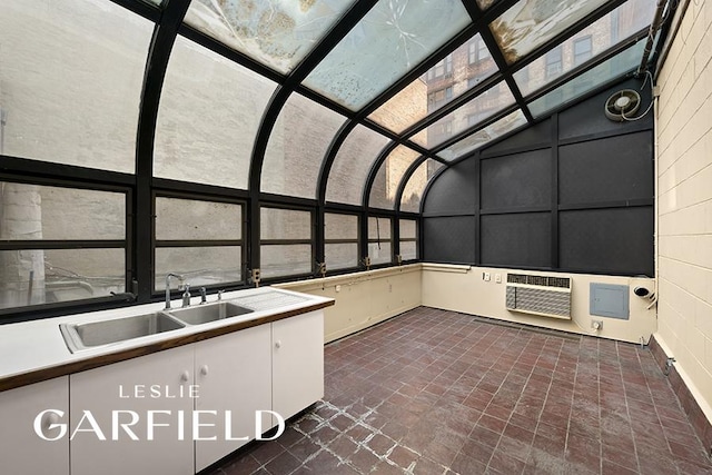 unfurnished sunroom with vaulted ceiling, a wealth of natural light, an AC wall unit, and a sink