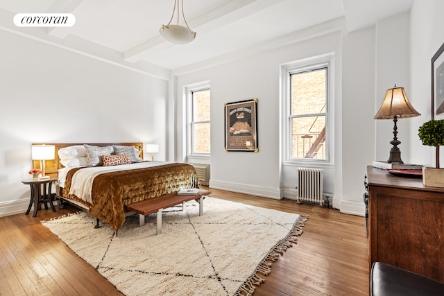 bedroom featuring light wood finished floors, radiator heating unit, visible vents, and beam ceiling